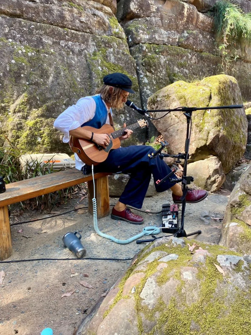 Solo acoustic musician performing outdoors near bushland on the South Coast